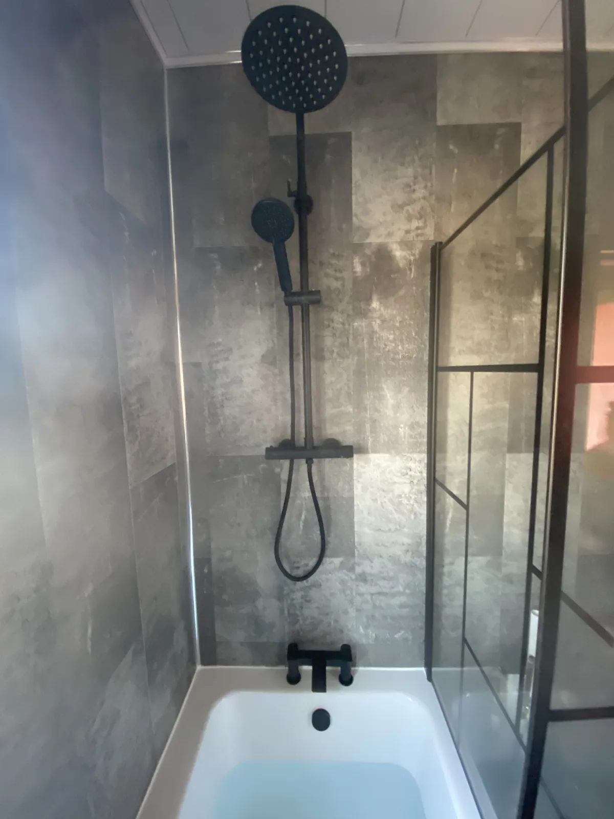 Tom’s bathroom installation with a black rainfall shower, matching bath taps and stone-effect wall panels
